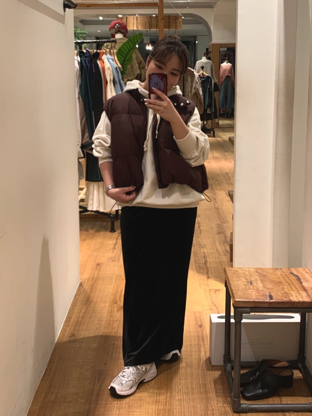 ブラウン系のダウンベスト、ホワイト系のパーカー、ブラック系のスカートを着用したレディースの秋コーディネートの1枚目の写真