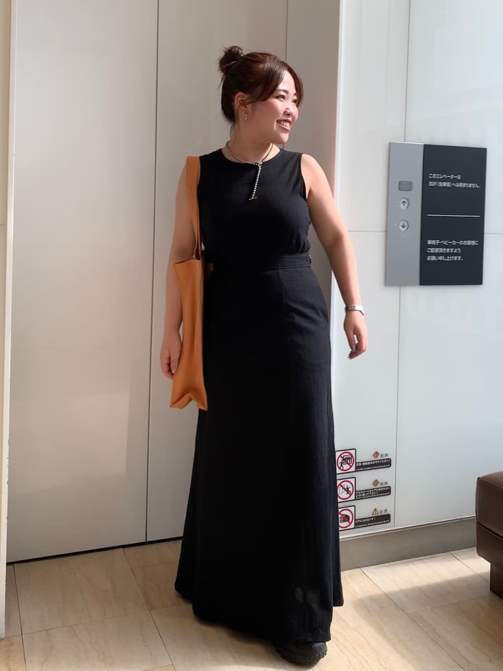 ブラック系のワンピース、オレンジ系のトートバッグを着用したレディースの春コーディネートの1枚目の写真