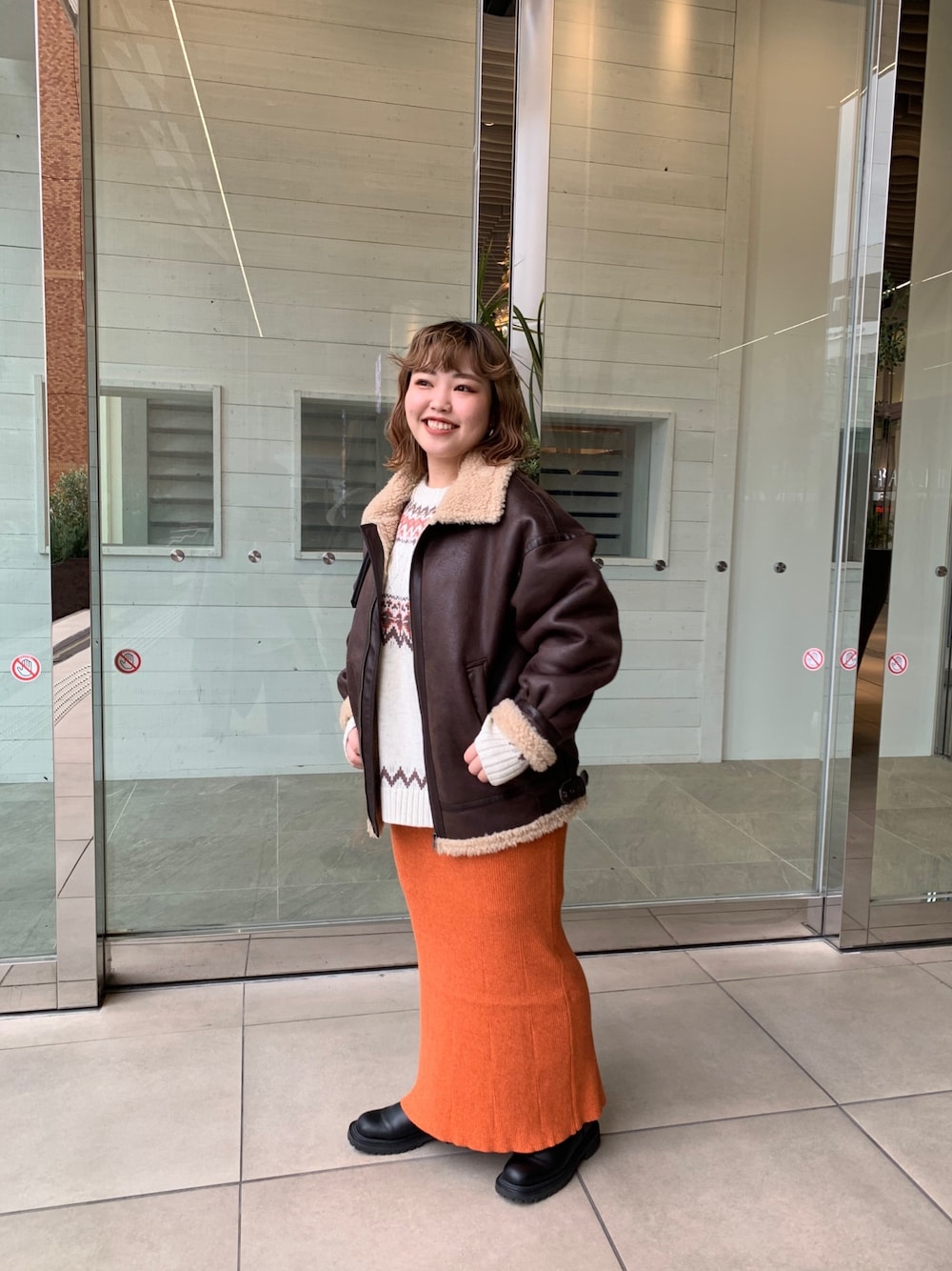 ブラウン系のムートンコート、オレンジ系のスカート、ホワイト系のニット/セーターを着用したレディースの冬コーディネートの1枚目の写真