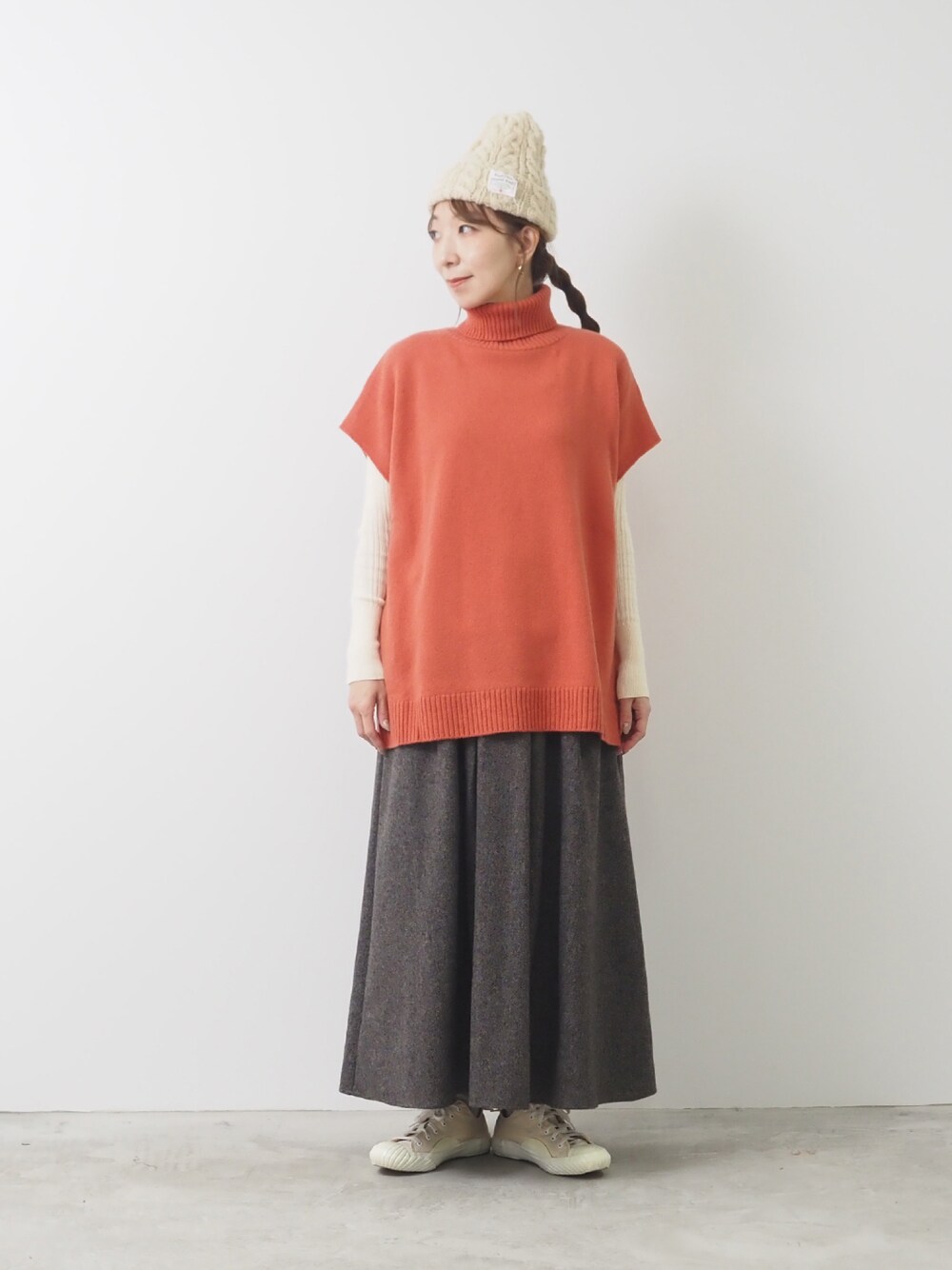 グリーン系のベスト、ブラウン系のスカートを着用したレディースの秋コーディネートの1枚目の写真