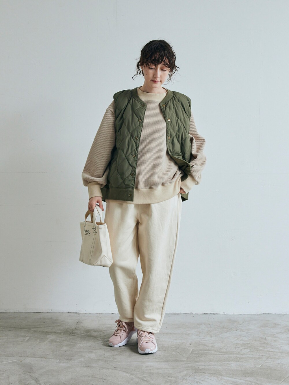 ベージュ系のスウェット、ホワイト系のデニムパンツ、グリーン系のベストを着用したレディースの秋コーディネートの1枚目の写真