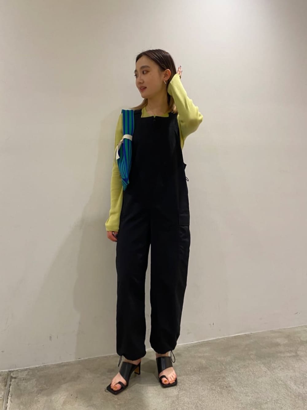 グリーン系のニット/セーター、ブラック系のサロペット/オーバーオール、グリーン系のショルダーバッグを着用したレディースの春コーディネートの1枚目の写真