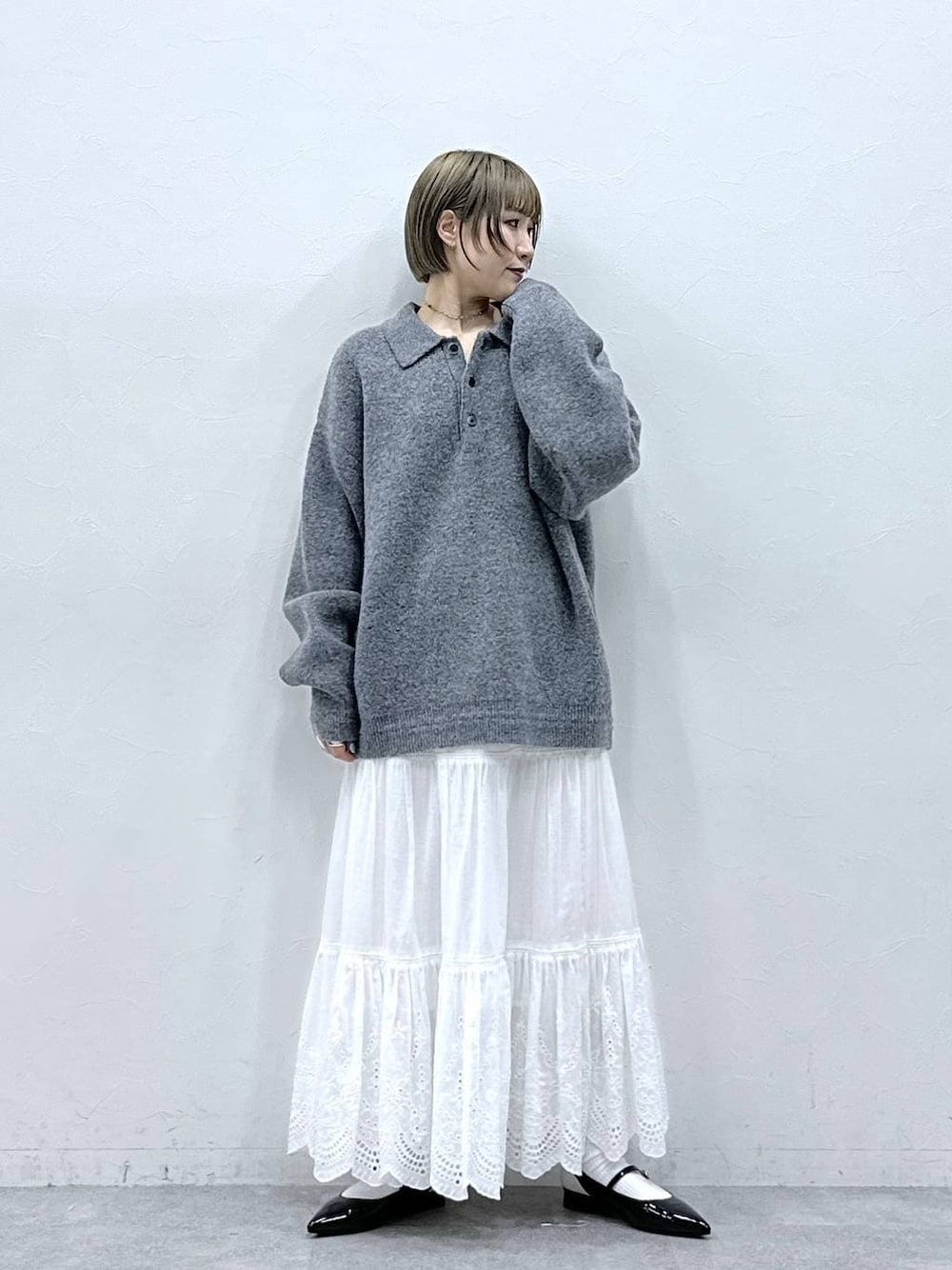 グレー系のポロシャツ、ホワイト系のスカート、ブラック系のパンプスを着用したレディースの冬コーディネートの1枚目の写真