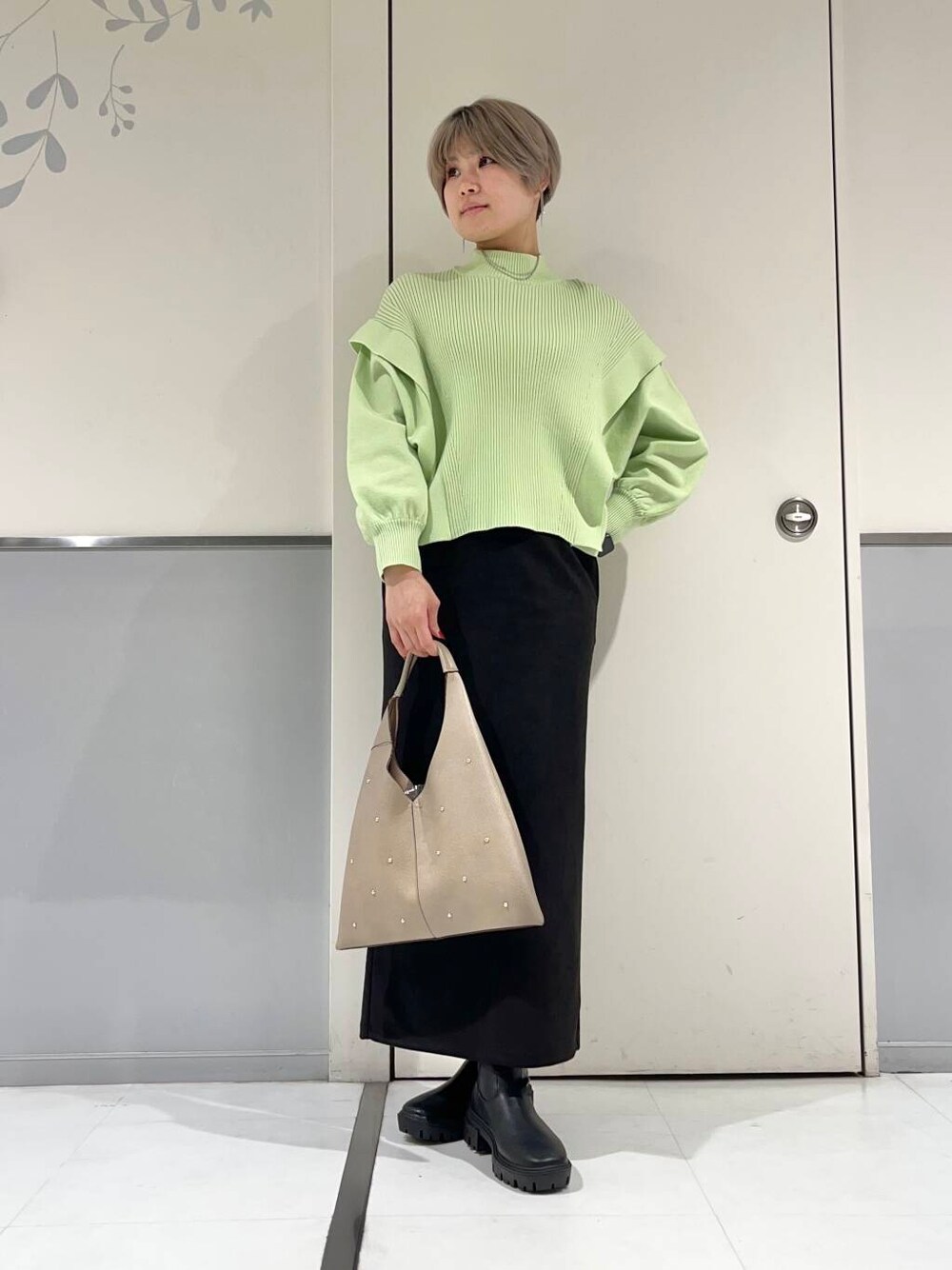 ベージュ系のトートバッグ、ブラック系のブーツ、グリーン系のニット/セーターを着用したレディースの冬コーディネートの1枚目の写真