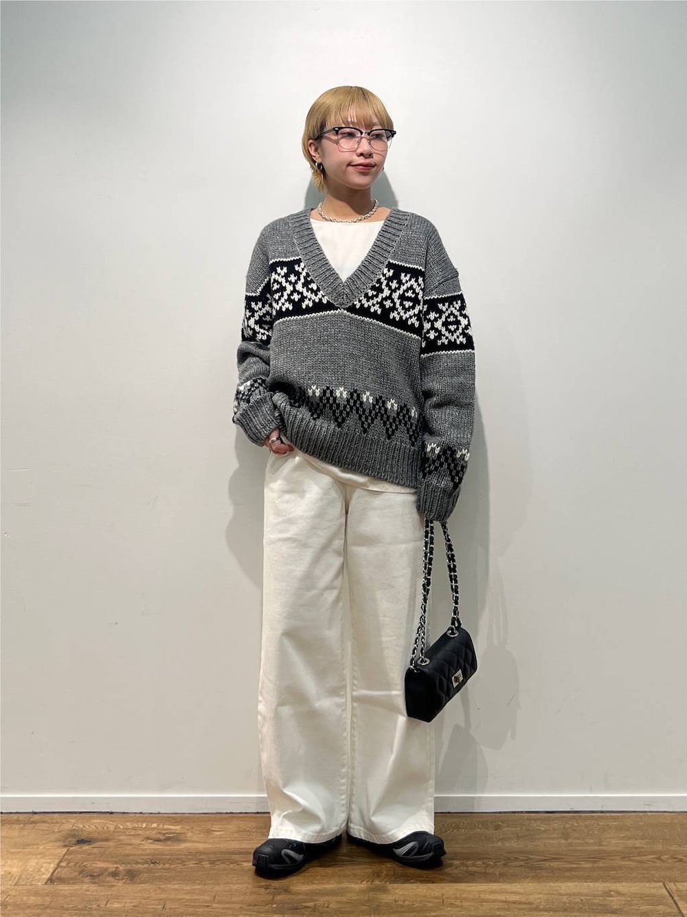 グレー系のニット/セーター、ブラック系のハンドバッグ、ホワイト系のデニムパンツを着用したレディースの秋コーディネートの1枚目の写真