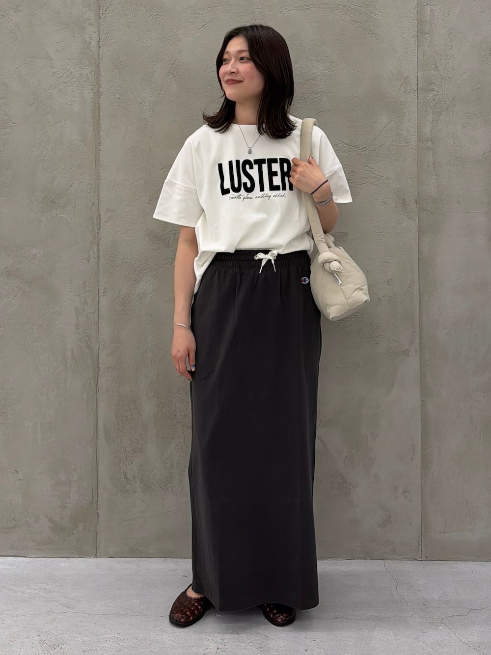 ブラック系のスカート、ホワイト系のTシャツ/カットソー、ベージュ系のショルダーバッグを着用したレディースの春コーディネートの1枚目の写真