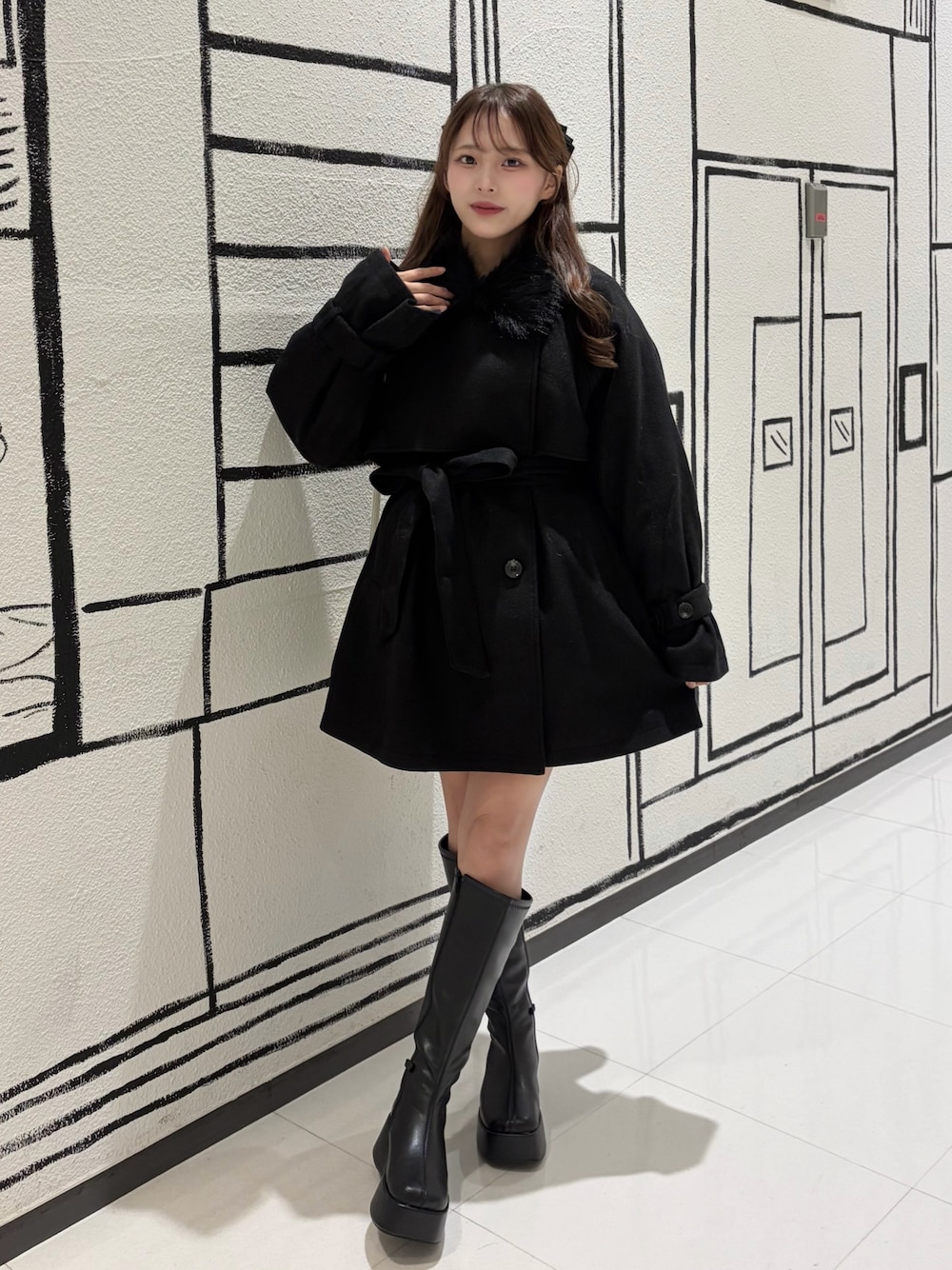 ブラック系のステンカラーコート、ブラック系のブーツを着用したレディースの秋コーディネートの1枚目の写真