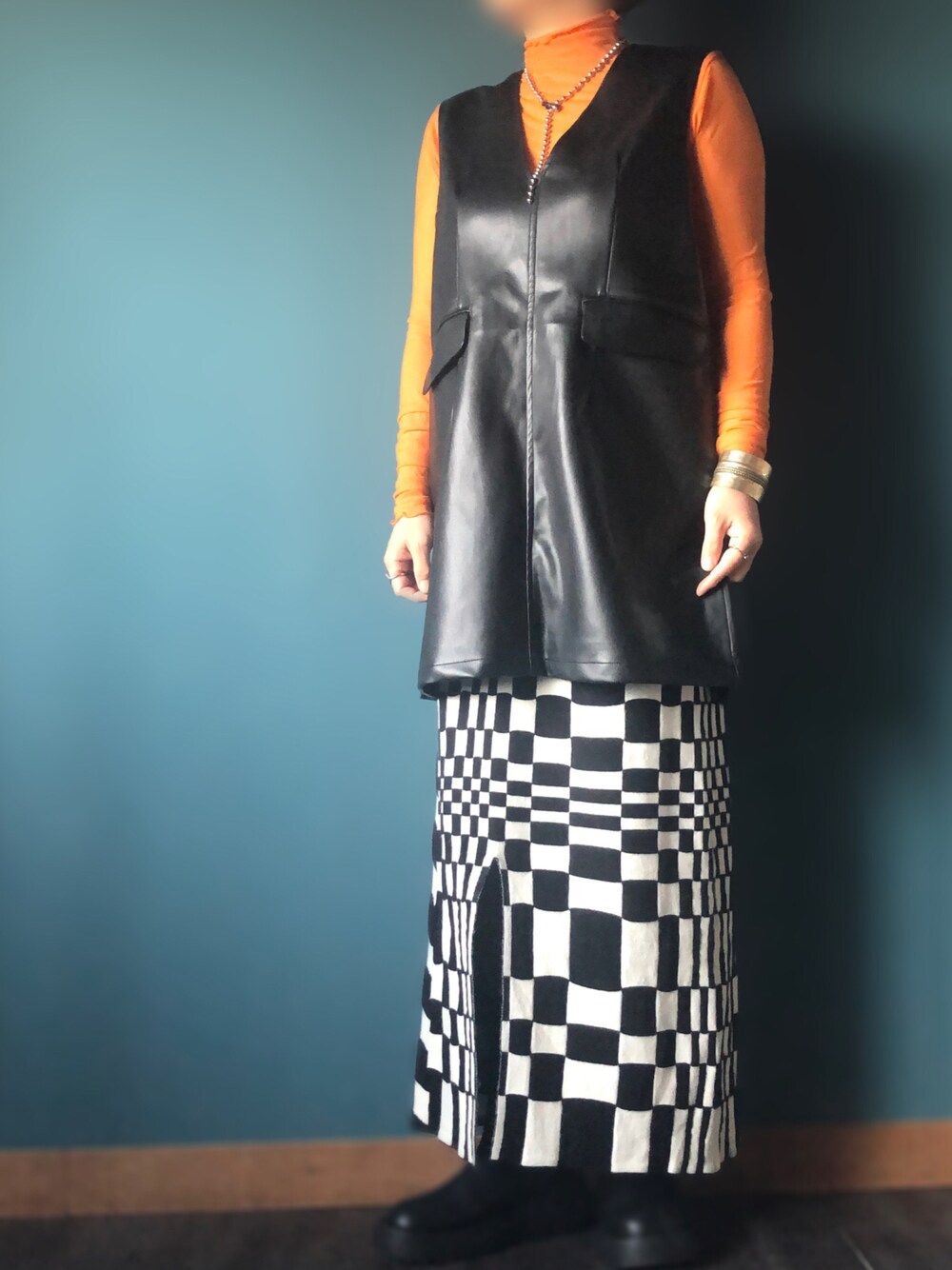 ブラック系のベスト、ブラック系のスカート、オレンジ系のTシャツ/カットソーを着用したレディースの冬コーディネートの1枚目の写真