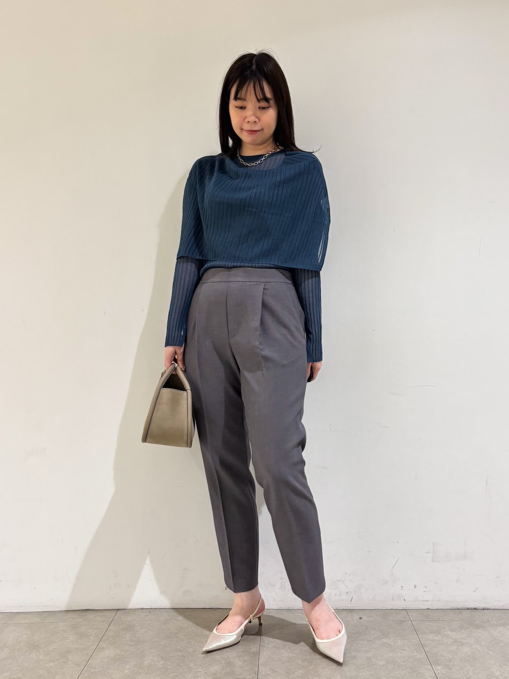 ブルー系のニット/セーター、グレー系のスラックスを着用したレディースの秋コーディネートの1枚目の写真