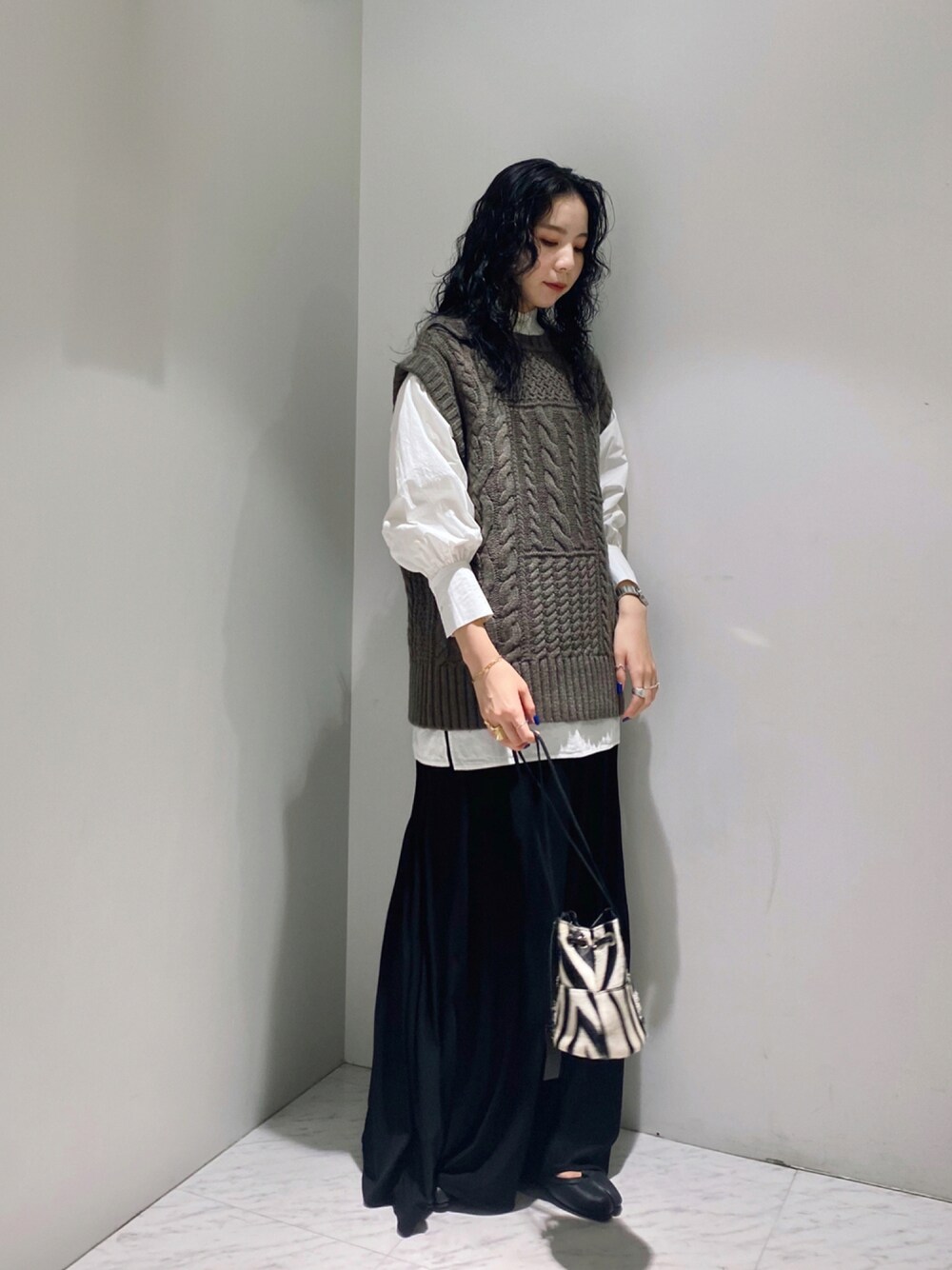 ブラウン系のニット/セーター、ホワイト系のシャツ/ブラウス、ブラック系のショルダーバッグを着用したレディースの秋コーディネートの1枚目の写真