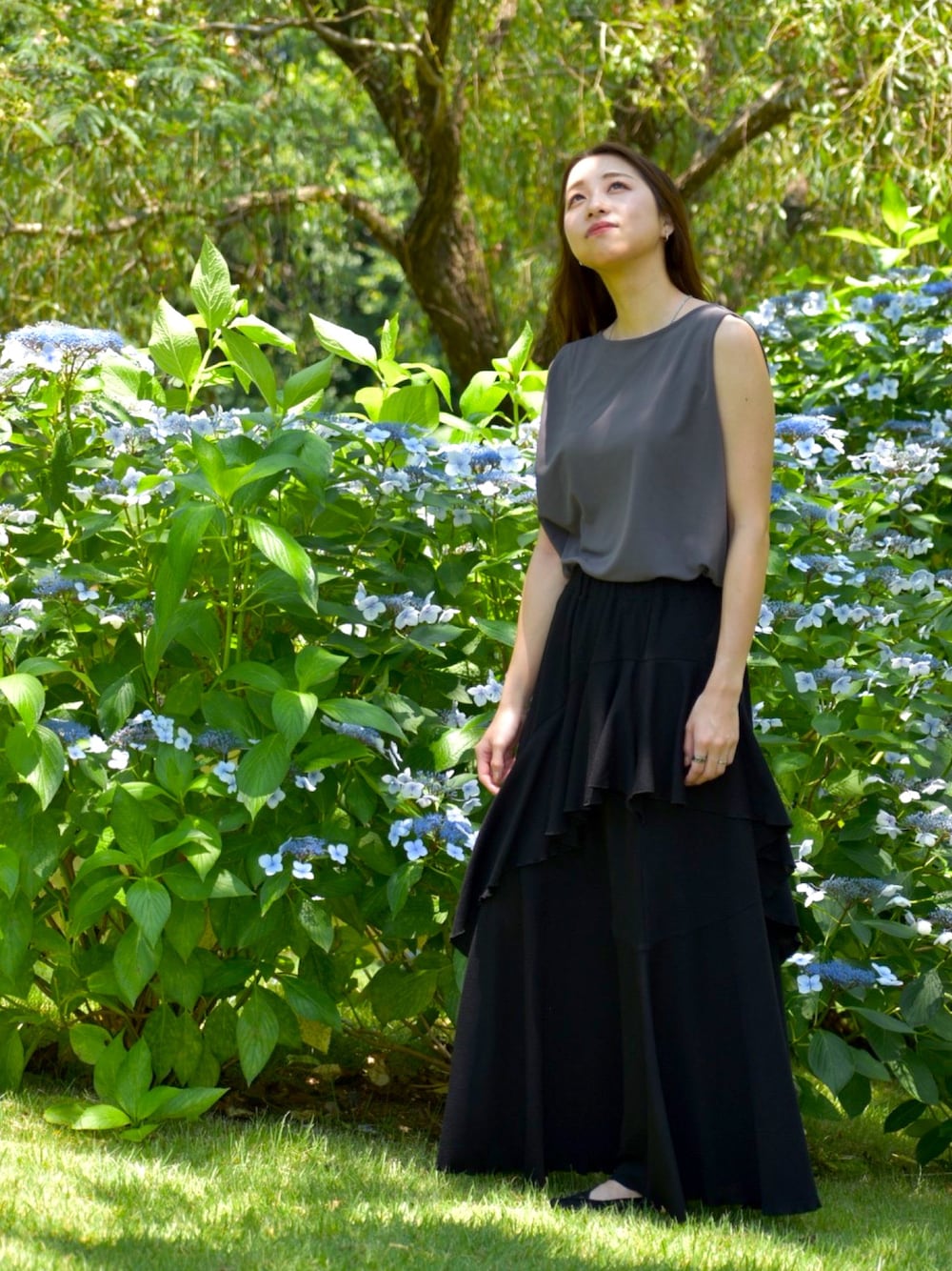 グレー系のトップス、ブラック系のスカート、ブラック系のパンプスを着用したレディースの夏コーディネートの1枚目の写真