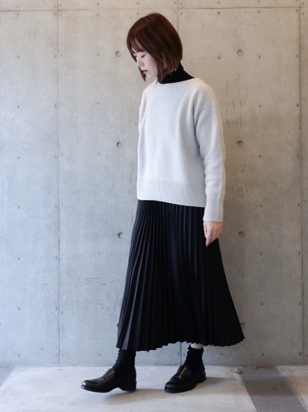 グレー系のニット/セーター、ブラック系のスカート、ブラック系のシューズを着用したレディースの冬コーディネートの1枚目の写真