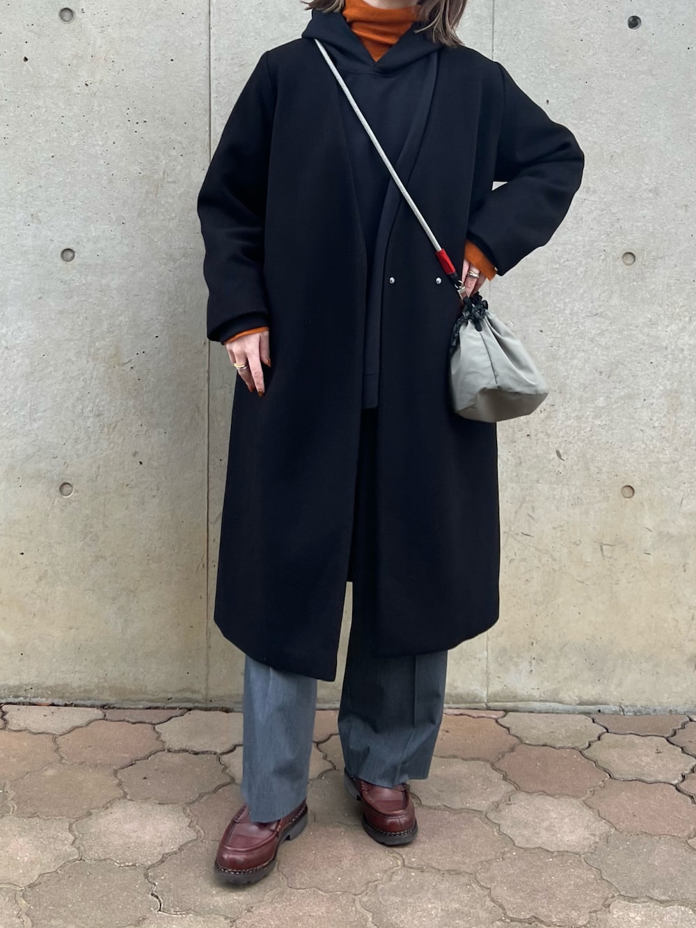 ブラック系のノーカラーコート、オレンジ系のニット/セーター、グレー系のショルダーバッグを着用したレディースの冬コーディネートの1枚目の写真