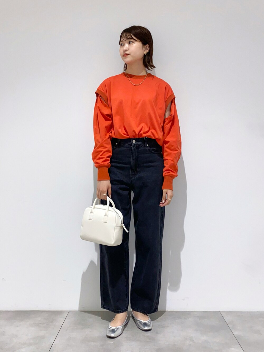 オレンジ系のTシャツ/カットソー、ホワイト系のボストンバッグ、ブラック系のデニムパンツを着用したレディースの秋コーディネートの1枚目の写真