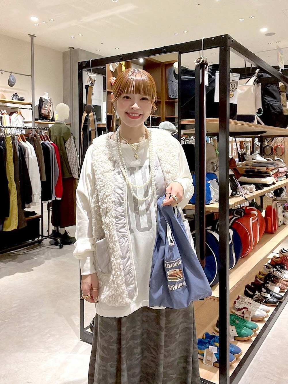 ベージュ系のベスト、その他のトートバッグ、グリーン系のスカートを着用したレディースの秋コーディネートの1枚目の写真