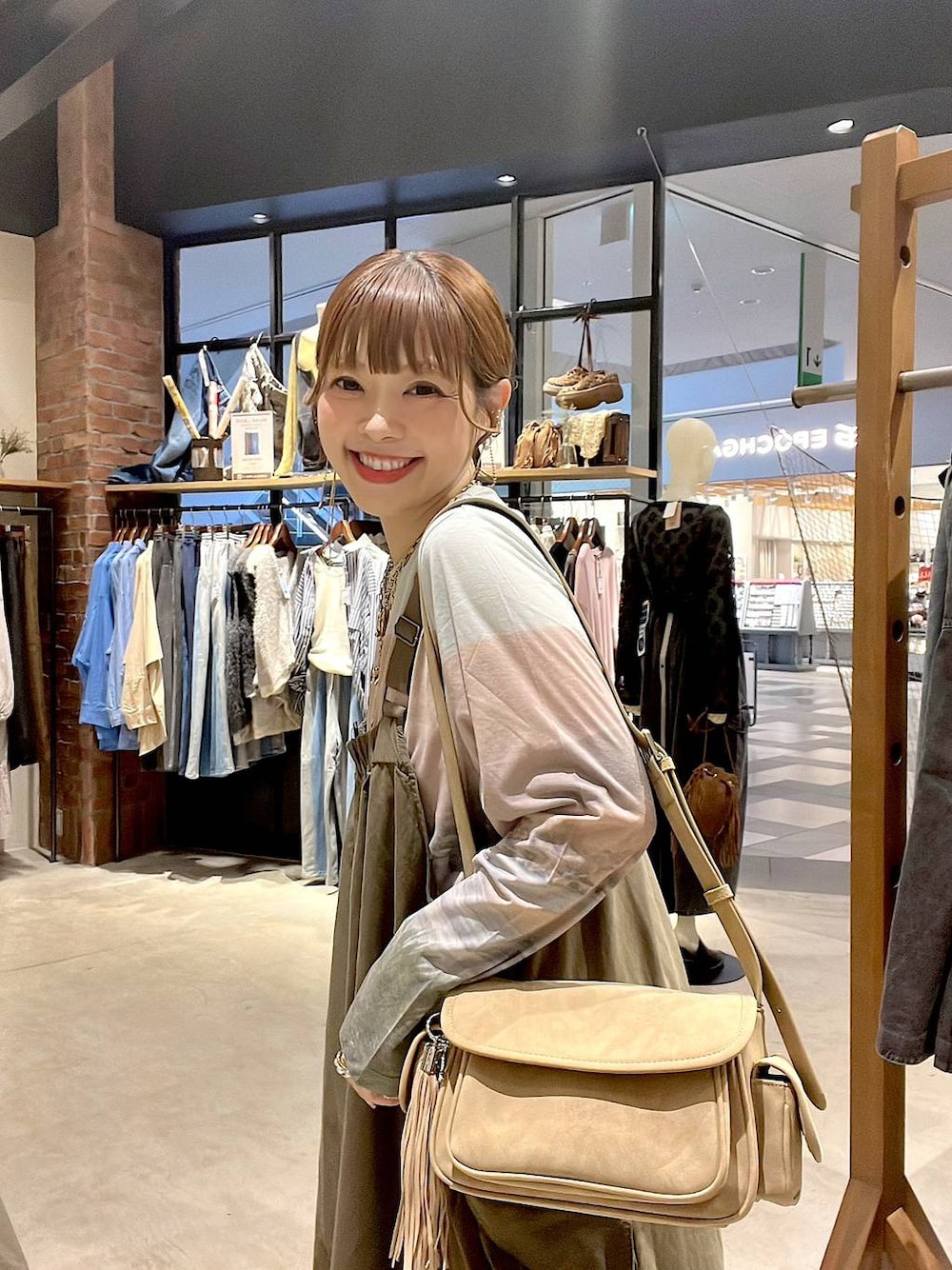 ベージュ系のTシャツ/カットソー、ベージュ系のショルダーバッグ、グリーン系のジャンパースカートを着用したレディースの夏コーディネートの1枚目の写真