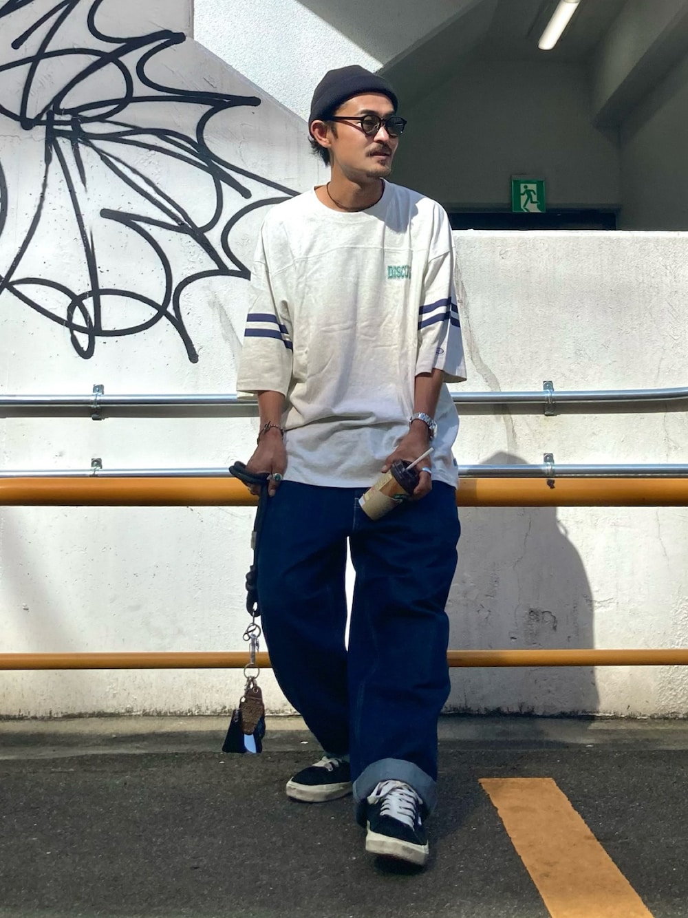 ベージュ系のTシャツ/カットソー、ブルー系のデニムパンツ、ブラック系のスニーカーを着用したメンズの秋コーディネートの1枚目の写真