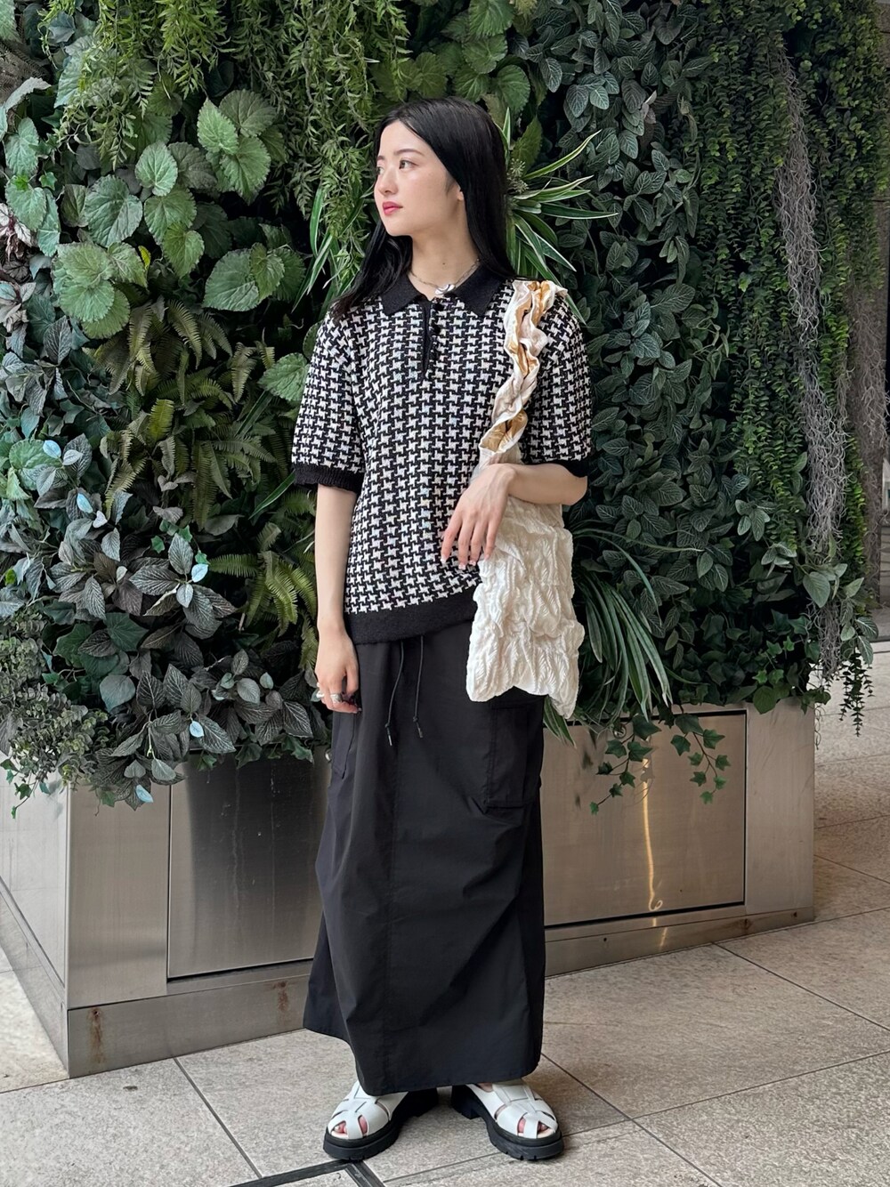 ブラック系のポロシャツ、ブラック系のスカート、ホワイト系のサンダルを着用したレディースの夏コーディネートの1枚目の写真