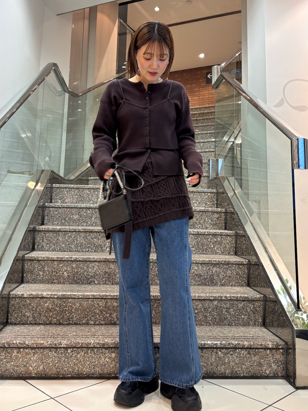 ブラウン系のニット/セーター、ブラウン系のスカート、ブルー系のデニムパンツを着用したレディースの冬コーディネートの1枚目の写真