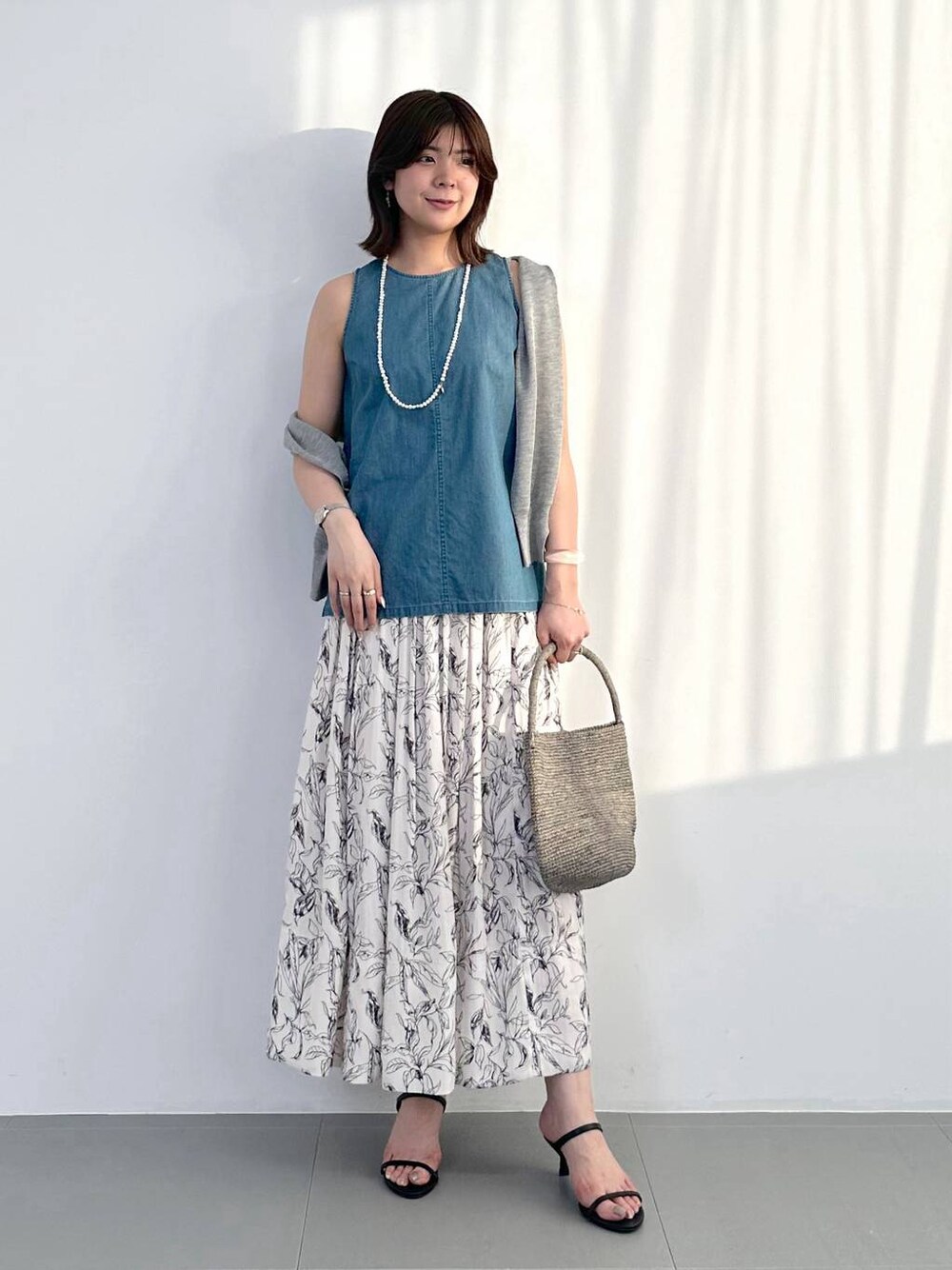 ブラック系のスリッポン、グレー系のトートバッグ、ホワイト系のスカートを着用したレディースの夏コーディネートの1枚目の写真