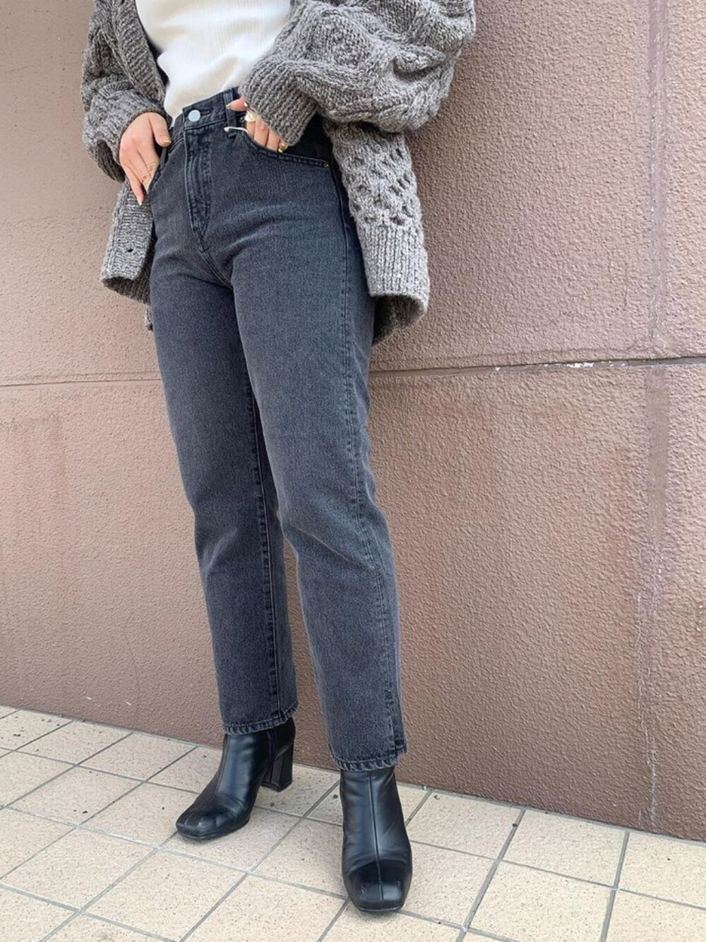 ブラック系のデニムパンツ、ブラウン系のカーディガン/ボレロ、ブラック系のブーツを着用したレディースの秋コーディネートの1枚目の写真