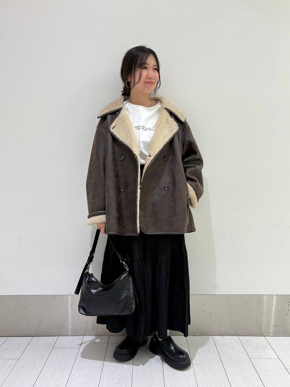 ブラウン系のムートンコート、ブラック系のショルダーバッグ、ブラック系のサンダルを着用したレディースの冬コーディネートの1枚目の写真