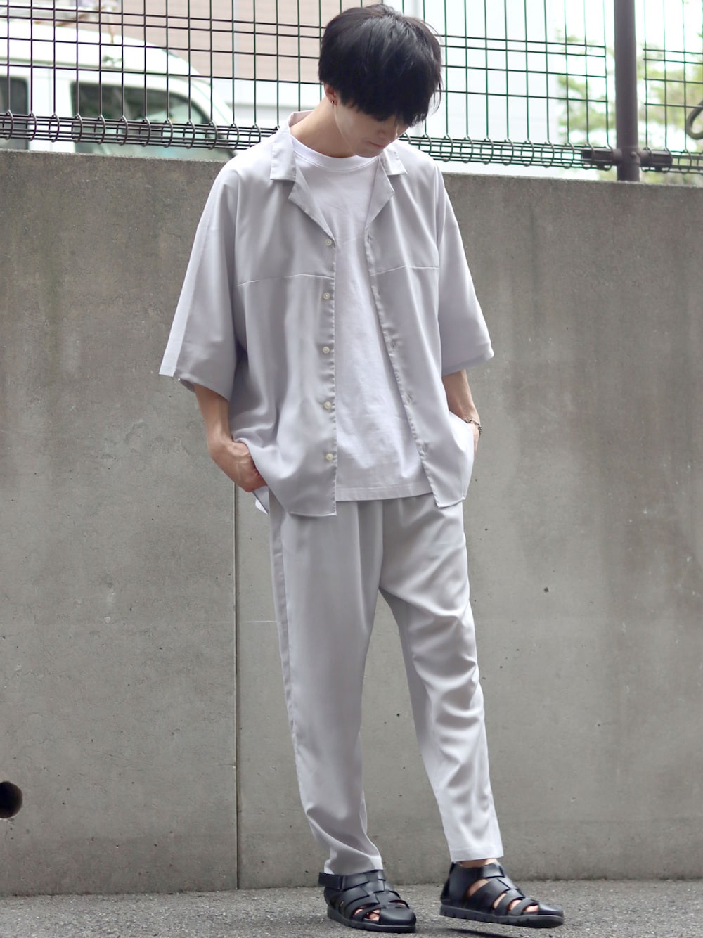 グレー系のセットアップ、ホワイト系のTシャツ/カットソー、ブラック系のサンダルを着用したメンズの夏コーディネートの1枚目の写真