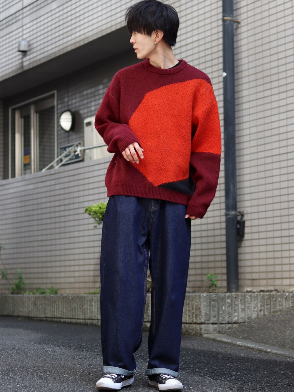 レッド系のニット/セーター、ブルー系のデニムパンツ、ブラック系のスニーカーを着用したメンズの秋コーディネートの1枚目の写真