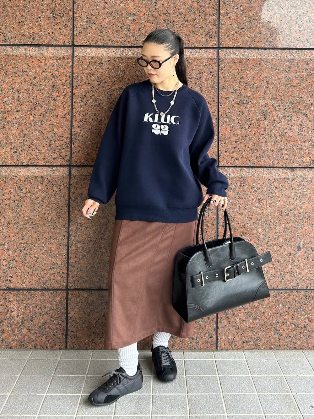 ブラウン系のスカート、ブラック系のショルダーバッグ、ブラック系のスニーカーを着用したレディースの秋コーディネートの1枚目の写真