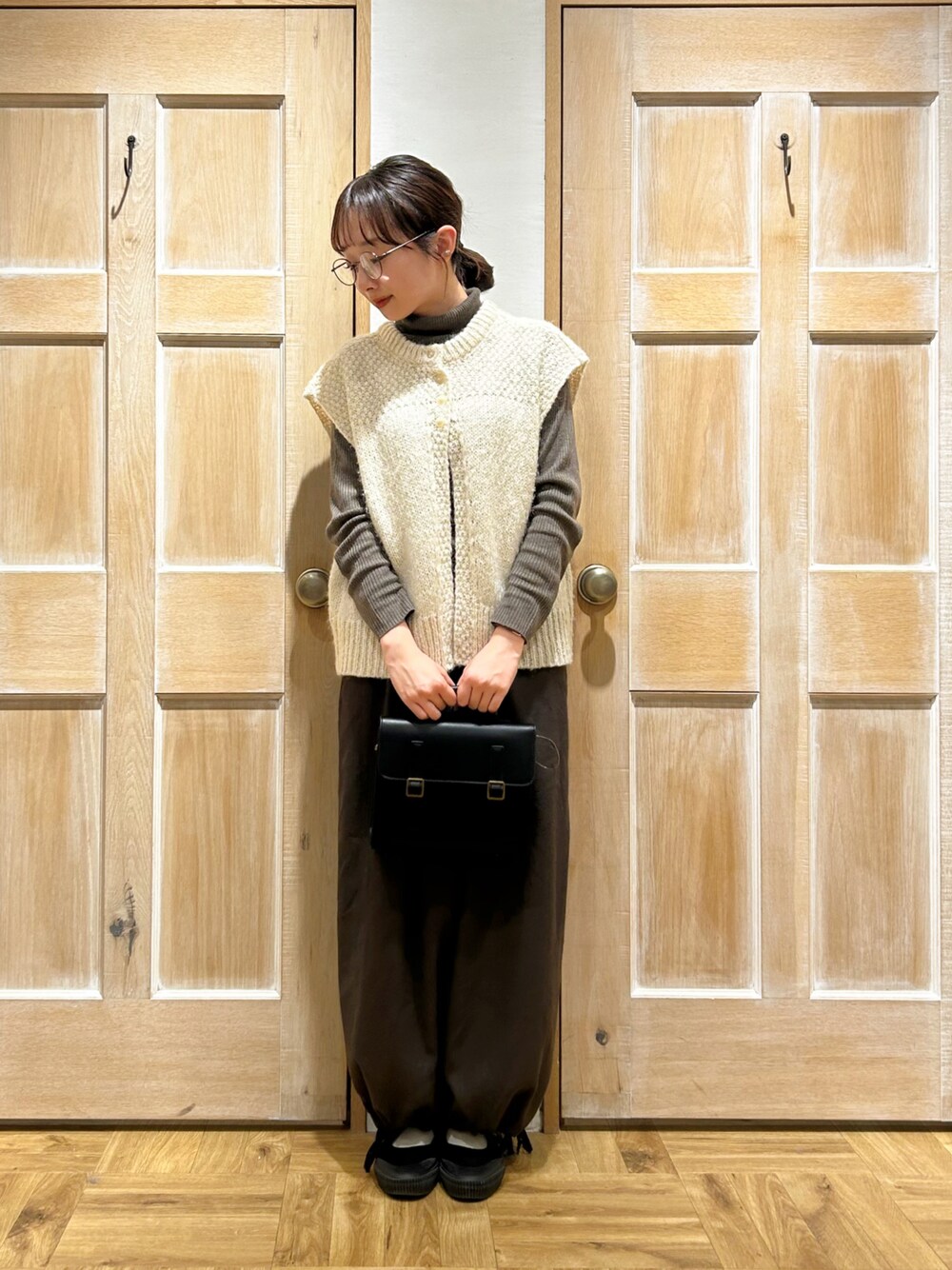 ホワイト系のベスト、ブラウン系のニット/セーター、ブラック系のハンドバッグを着用したレディースの冬コーディネートの1枚目の写真