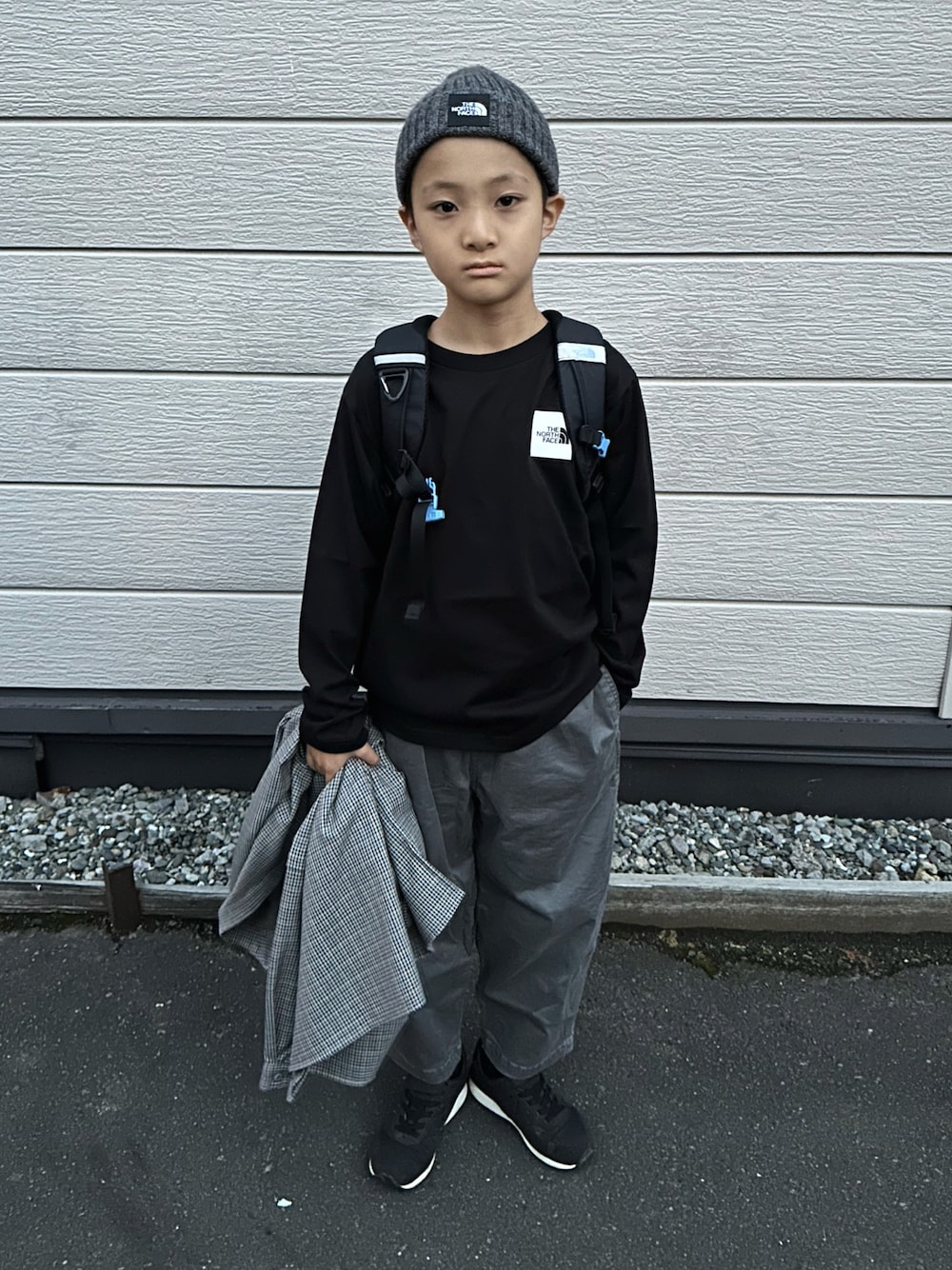 ブラック系のTシャツ/カットソー、ブラック系のバックパック/リュック、グレー系のチノパンツを着用したキッズの秋コーディネートの1枚目の写真