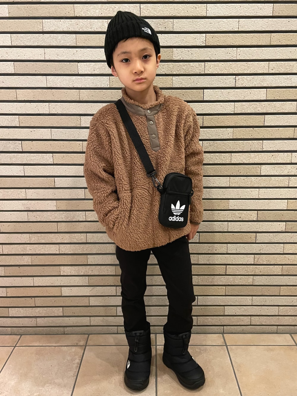 ブラウン系のその他トップス、ブラック系のパンツ、ブラック系のショルダーバッグを着用したキッズの冬コーディネートの1枚目の写真