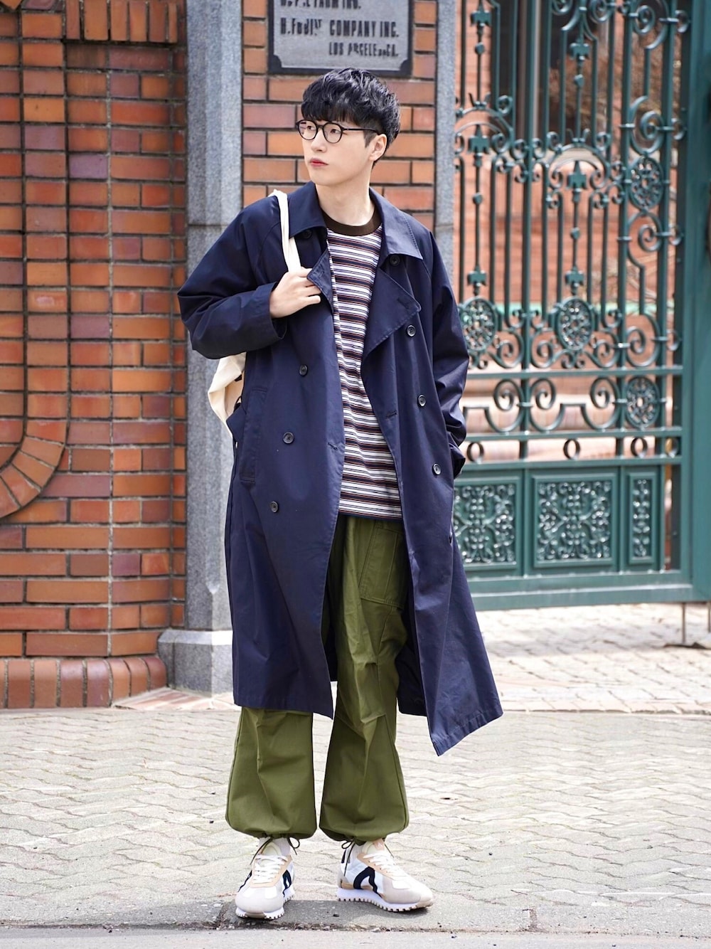 ブラック系のトレンチコート、ホワイト系のトートバッグ、ブラウン系のTシャツ/カットソーを着用したメンズの春コーディネートの1枚目の写真