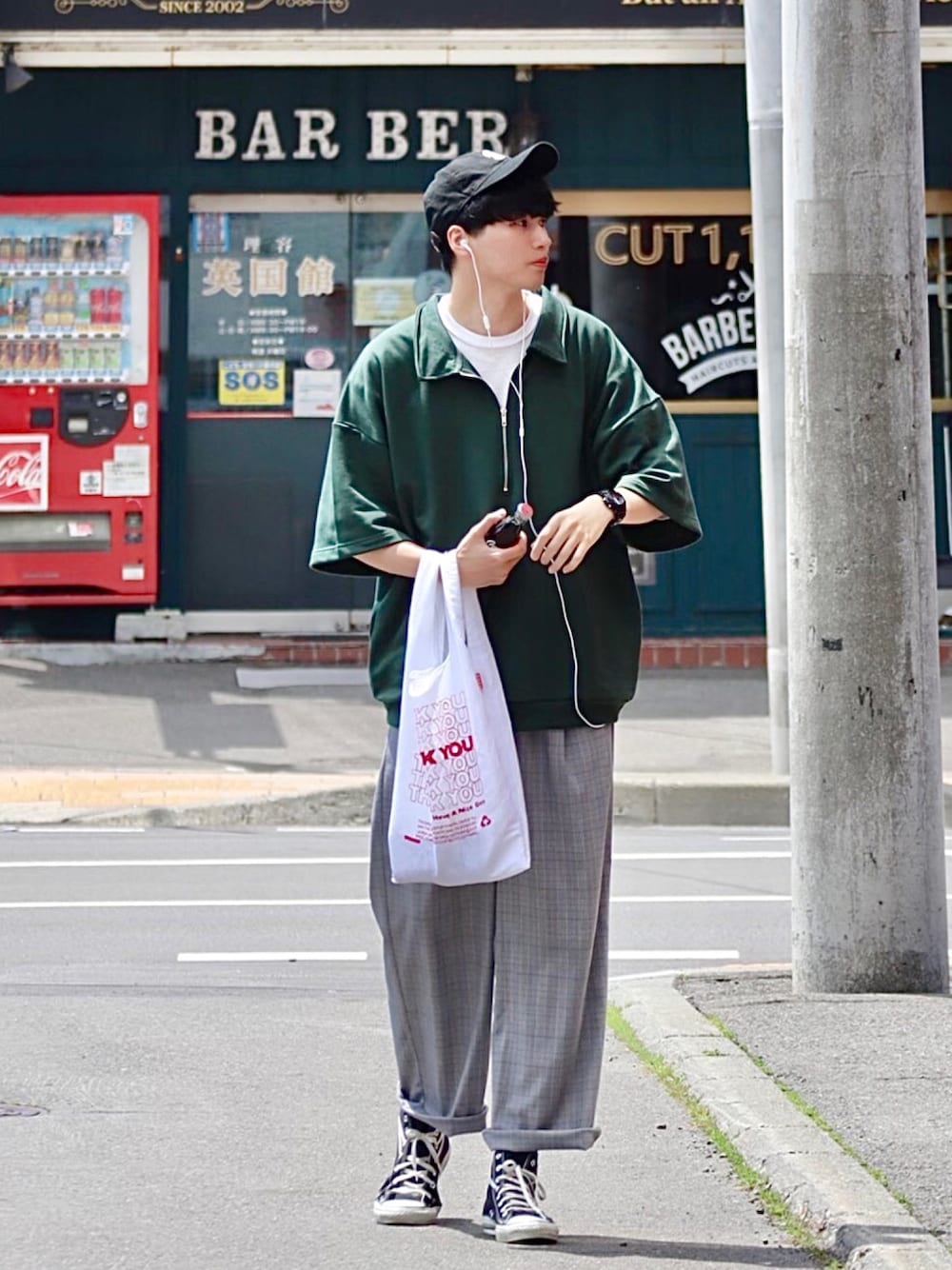 グリーン系のポロシャツ、ホワイト系のエコバッグ/サブバッグ、グレー系のスラックスを着用したメンズの夏コーディネートの1枚目の写真