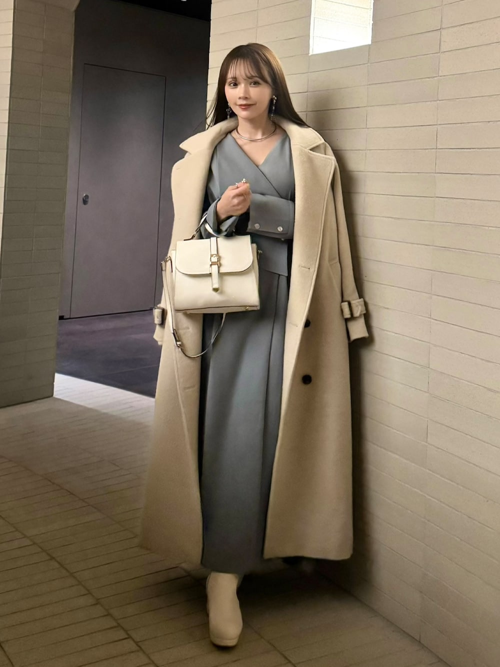 グレー系のワンピース、ホワイト系のステンカラーコート、ホワイト系のブーツを着用したレディースの冬コーディネートの1枚目の写真