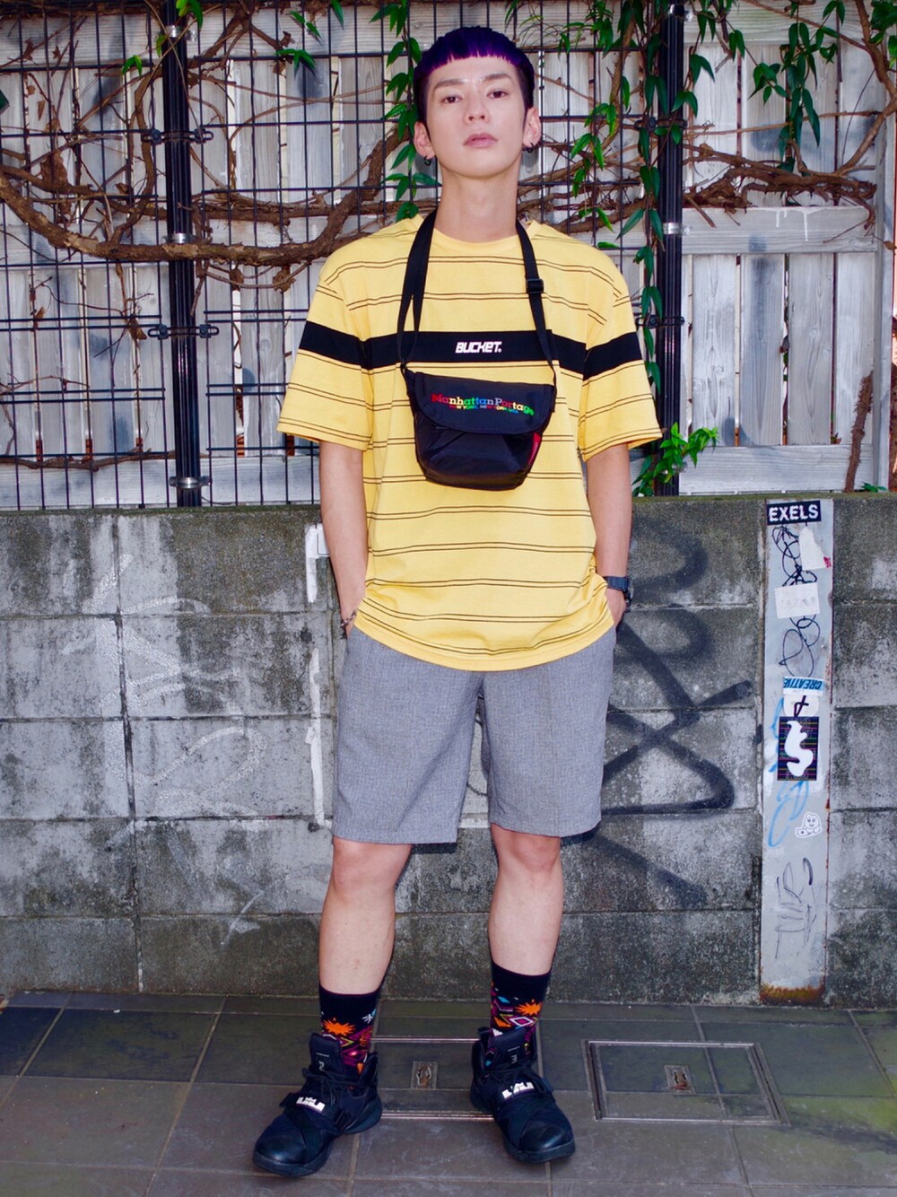 ブラック系のメッセンジャーバッグ、イエロー系のTシャツ/カットソー、ブラック系のスニーカーを着用したメンズの夏コーディネートの1枚目の写真