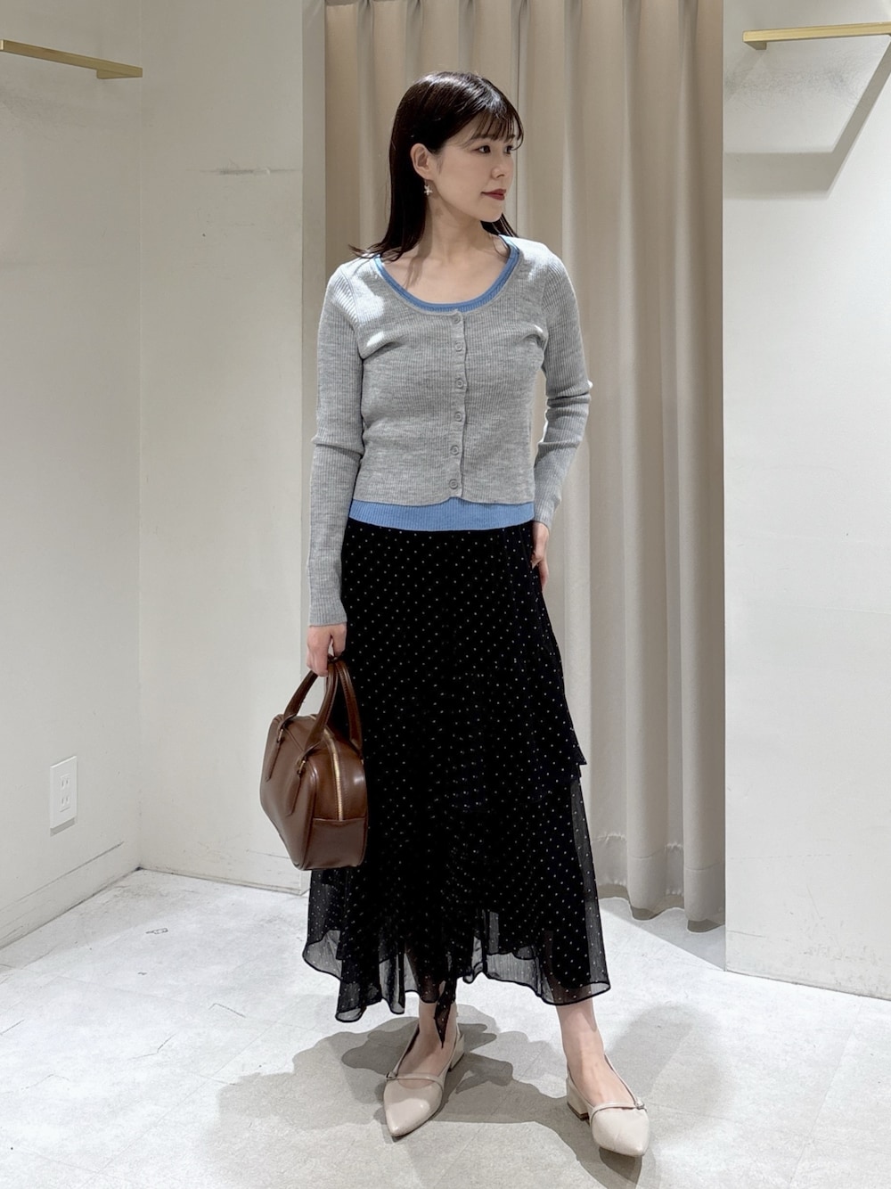 グレー系のニット/セーター、ブラック系のスカート、ブラウン系のハンドバッグを着用したレディースの春コーディネートの1枚目の写真