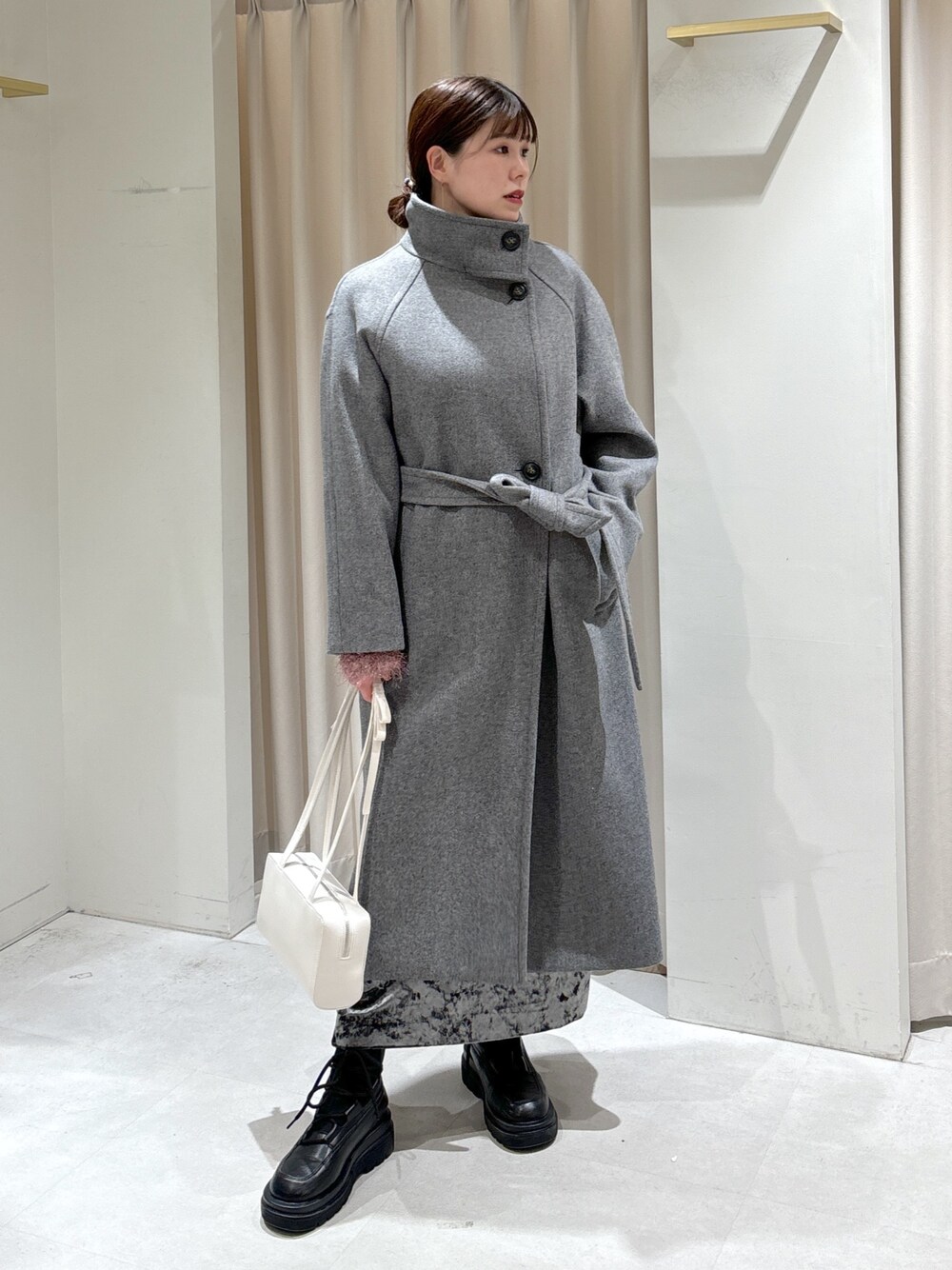 グレー系のステンカラーコート、ホワイト系のショルダーバッグ、ブラック系のブーツを着用したレディースの冬コーディネートの1枚目の写真