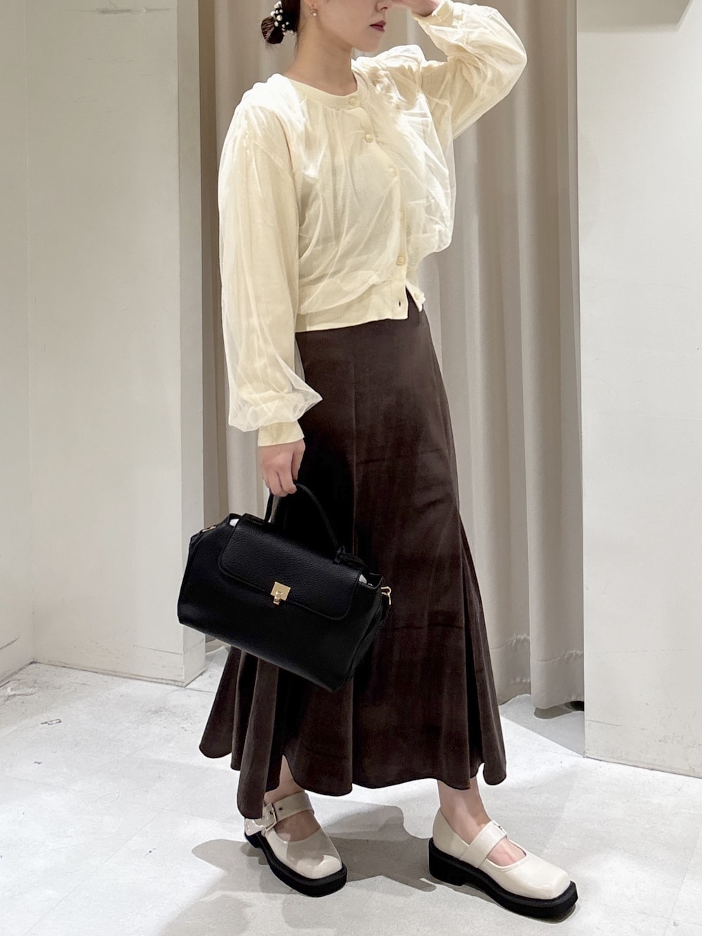 イエロー系のニット/セーター、ブラウン系のスカート、ブラック系のショルダーバッグを着用したレディースの冬コーディネートの1枚目の写真