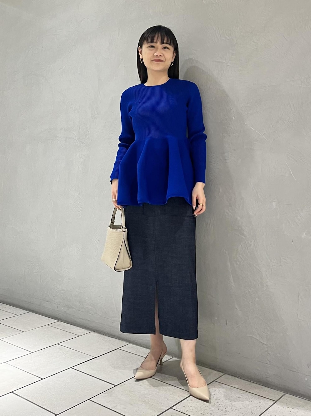 ベージュ系のパンプス、ベージュ系のショルダーバッグ、ブルー系のニット/セーターを着用したレディースの冬コーディネートの1枚目の写真