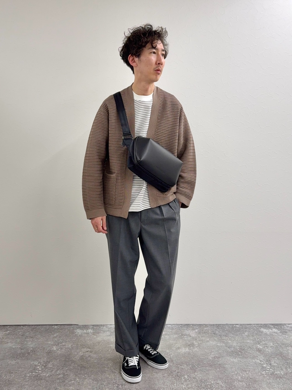 ブラック系のショルダーバッグ、ホワイト系のTシャツ/カットソー、グレー系のスラックスを着用したメンズの春コーディネートの1枚目の写真