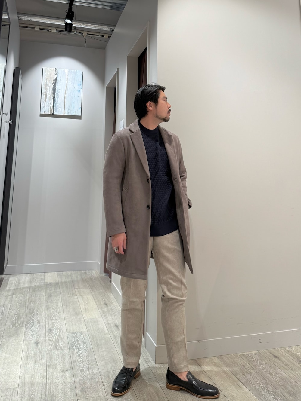 ブラウン系のチェスターコート、ブルー系のニット/セーター、ベージュ系のスラックスを着用したメンズの冬コーディネートの1枚目の写真