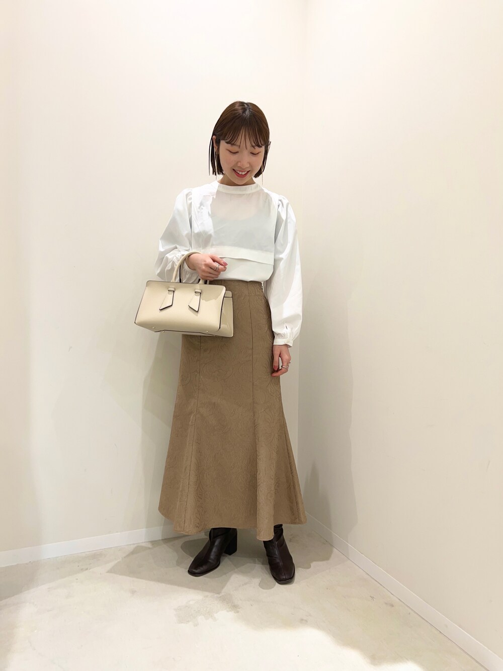 ベージュ系のスカート、ブラウン系のブーツ、ホワイト系のTシャツ/カットソーを着用したレディースの冬コーディネートの1枚目の写真