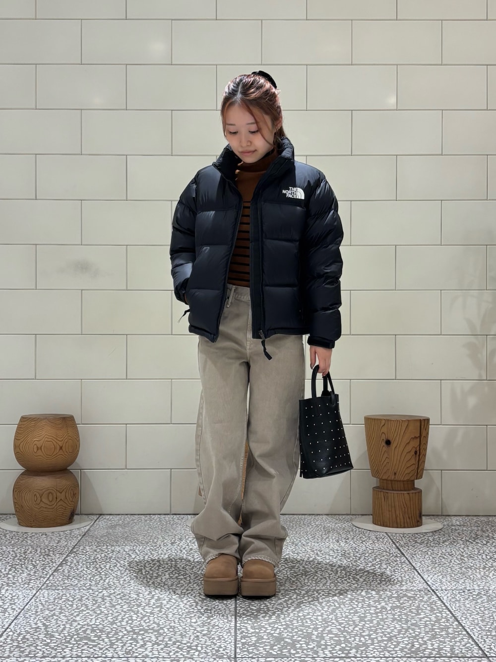 ブラウン系のニット/セーター、ブラック系のダウンジャケット/コート、ベージュ系のデニムパンツを着用したレディースの秋コーディネートの1枚目の写真