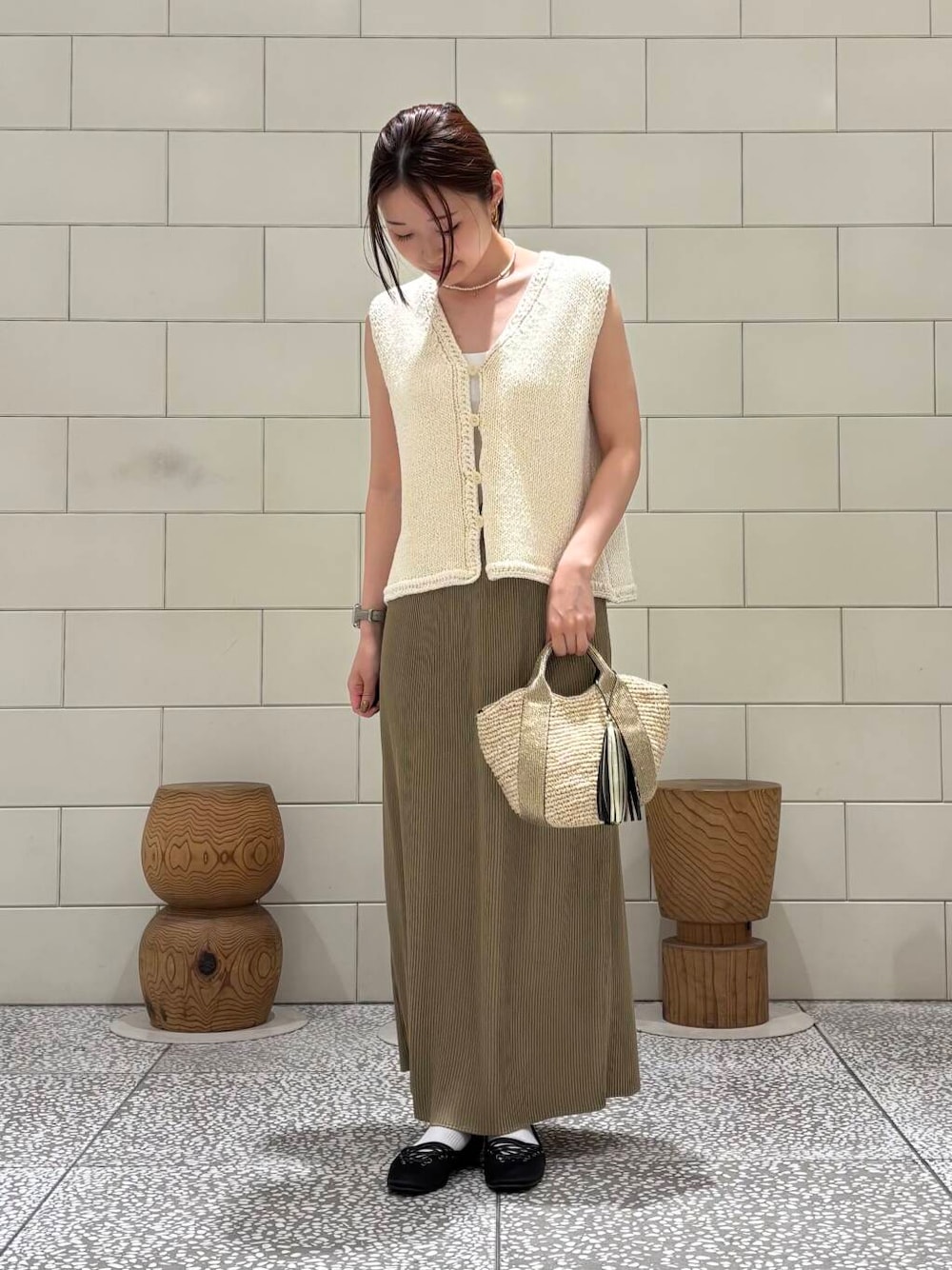 ゴールド系のかごバッグ、ホワイト系のベスト、ベージュ系のスカートを着用したレディースの夏コーディネートの1枚目の写真