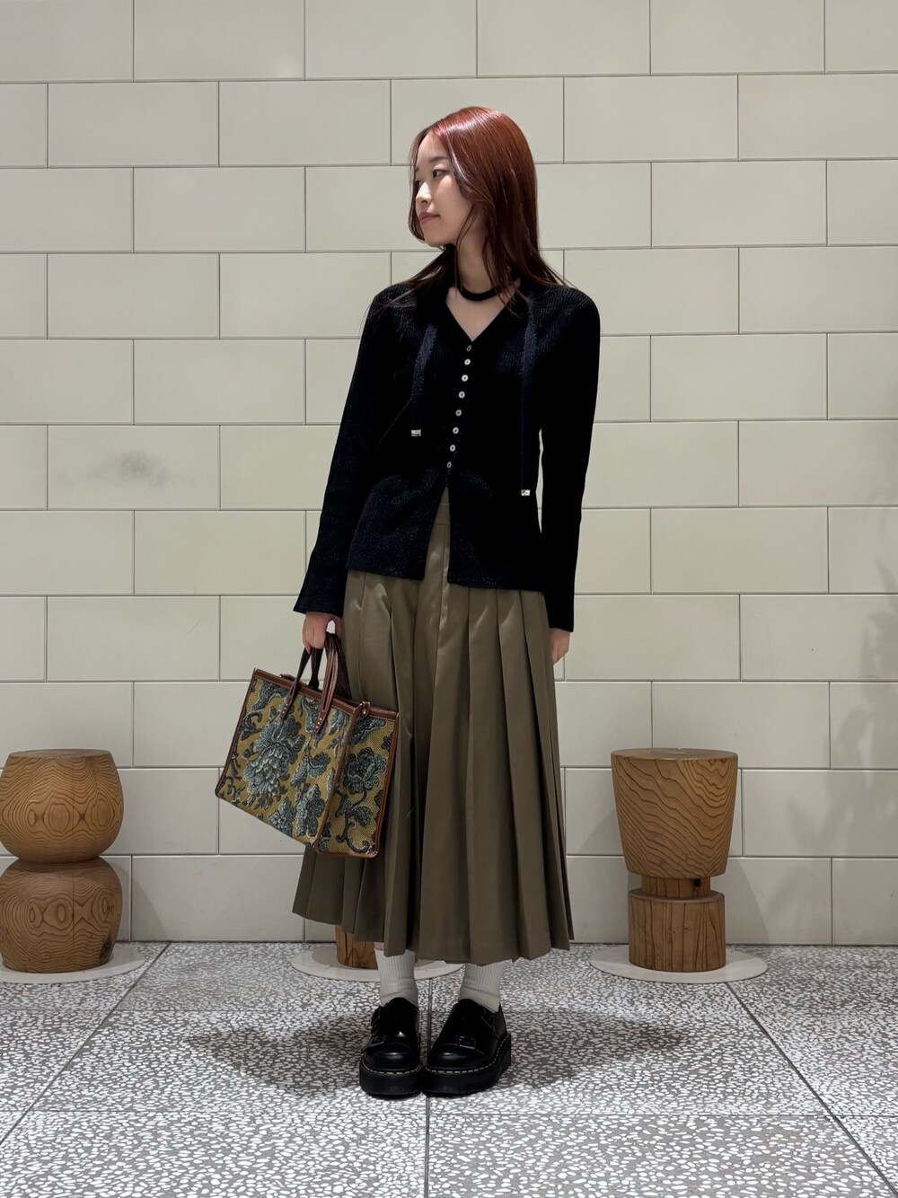 ブラック系のカーディガン/ボレロ、グリーン系のスカート、ブラウン系のハンドバッグを着用したレディースの秋コーディネートの1枚目の写真