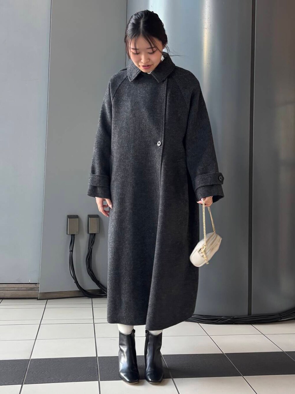 ブラック系のステンカラーコート、ホワイト系のショルダーバッグ、ブラウン系のスカートを着用したレディースの冬コーディネートの1枚目の写真