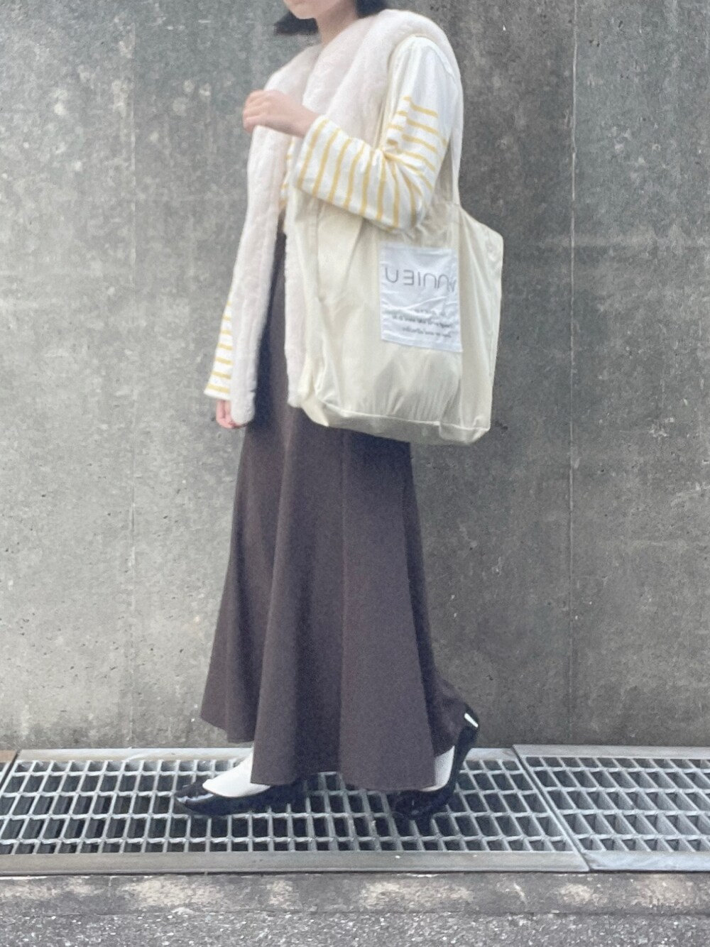 イエロー系のTシャツ/カットソー、ホワイト系のベスト、ブラウン系のスカートを着用したレディースの冬コーディネートの1枚目の写真