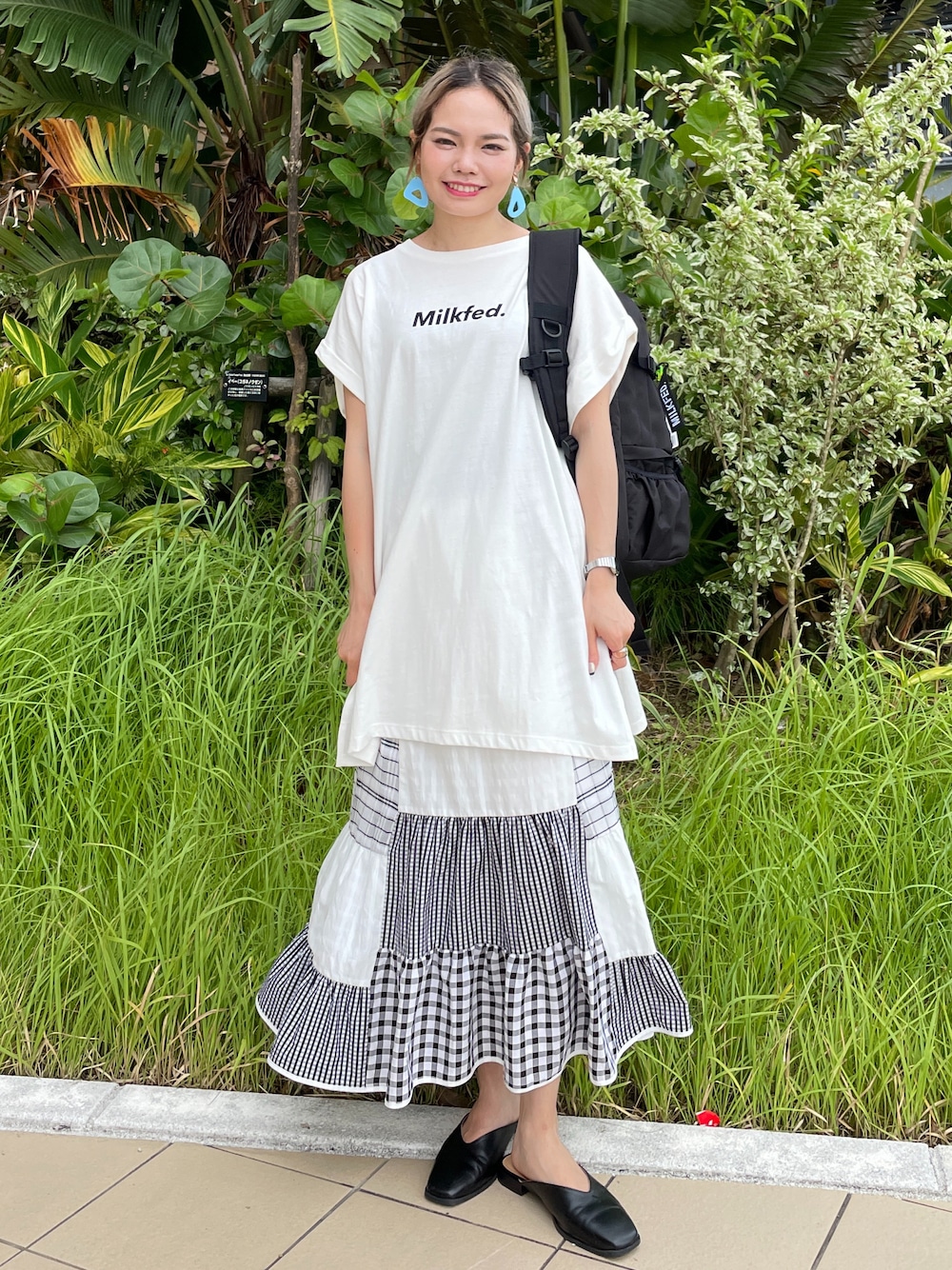 グリーン系のスカート、ホワイト系のTシャツ/カットソー、ブラック系のバックパック/リュックを着用したレディースの夏コーディネートの1枚目の写真