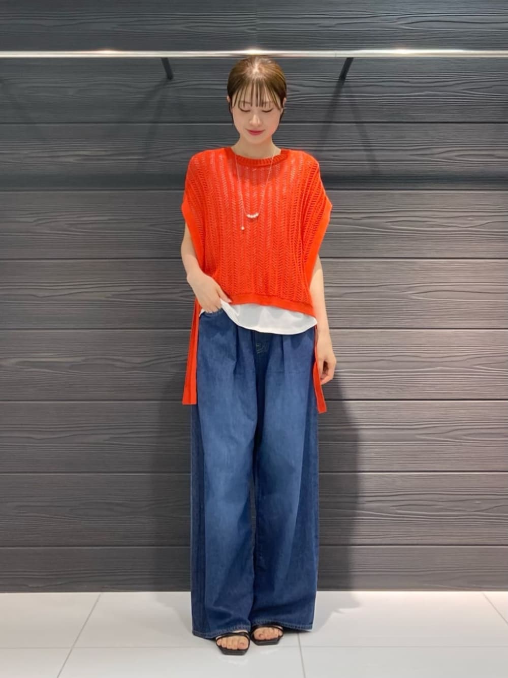 オレンジ系のアンサンブル、ブルー系のデニムパンツ、ホワイト系のネックレスを着用したレディースの夏コーディネートの1枚目の写真